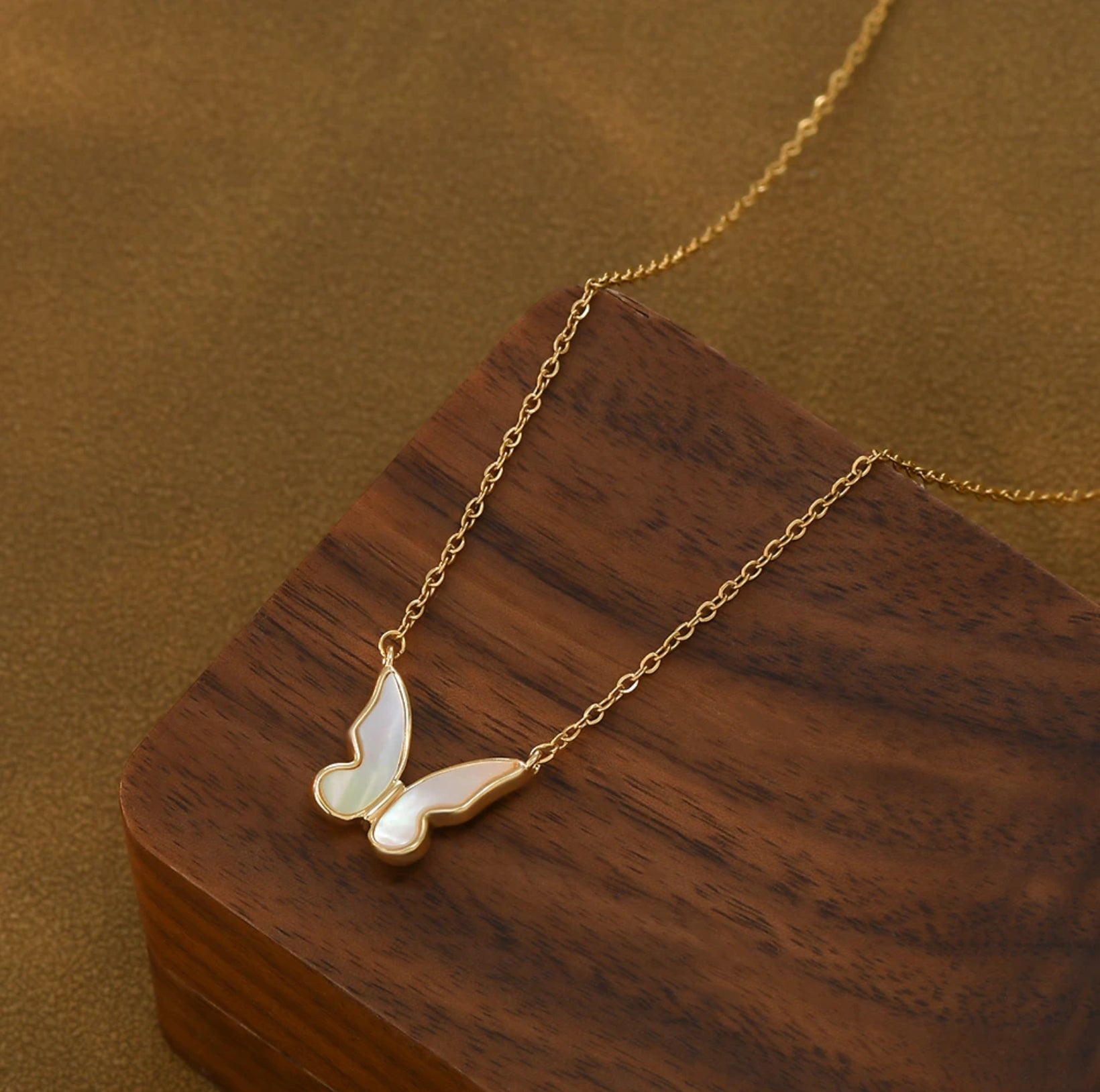 Close-up of the Shell Butterfly Necklace showing delicate mother of pearl inlay in a gold butterfly pendant on an adjustable chain, shown on wooden box.