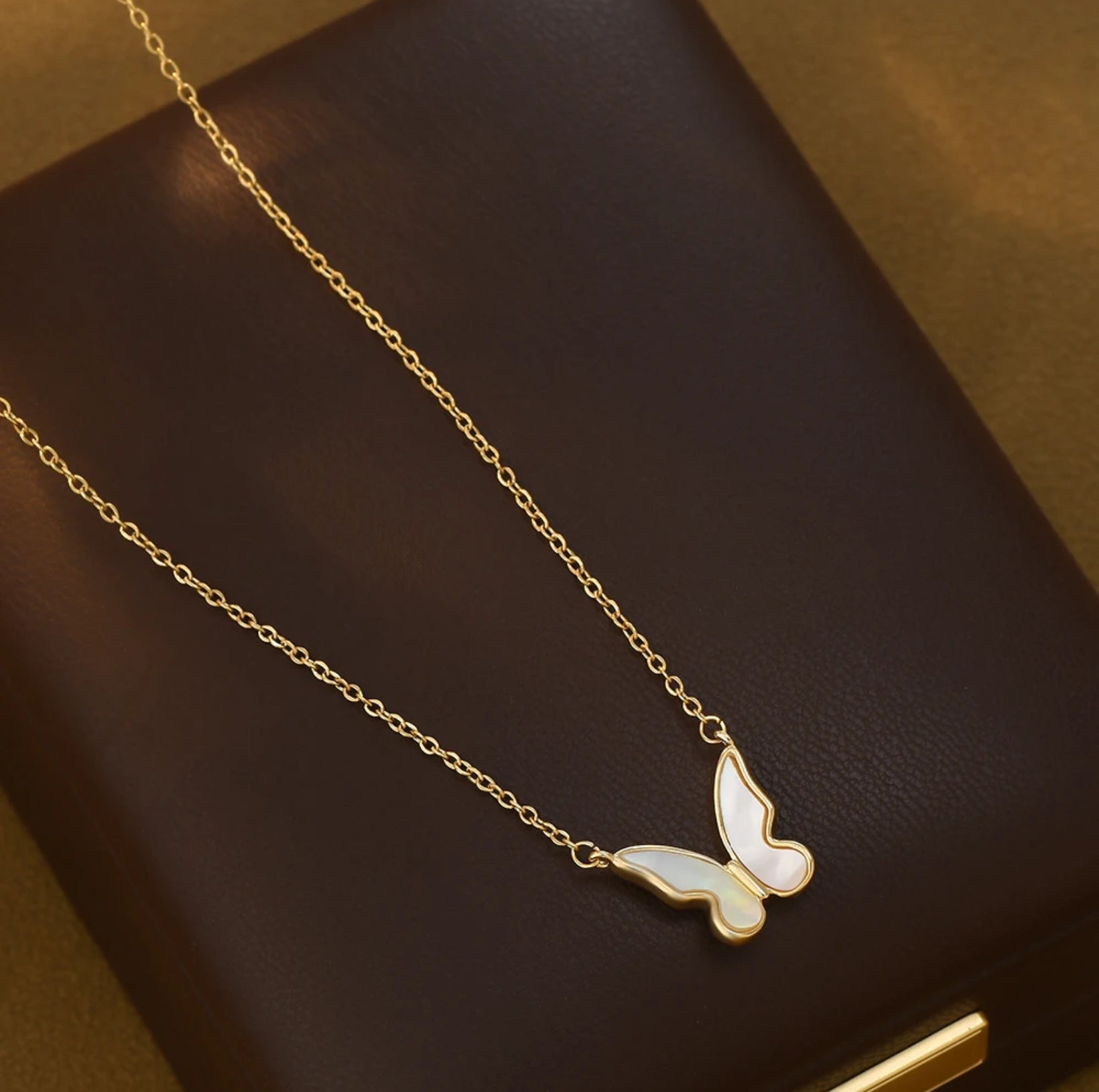 Close-up of the Shell Butterfly Necklace showing delicate mother of pearl inlay in a gold butterfly pendant on an adjustable chain, shown on leather box.