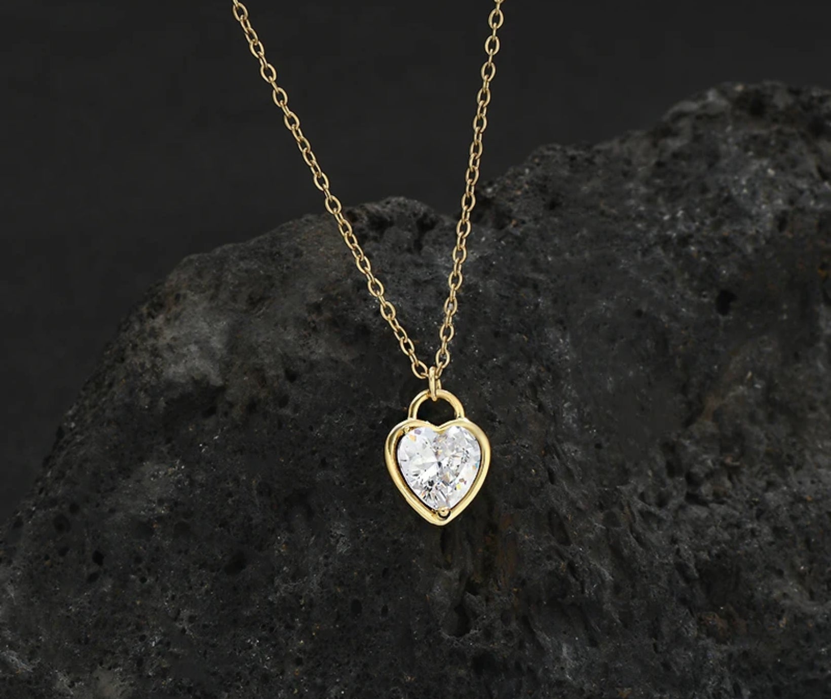 Super close-up of the Zircon Heart Locket Necklace showing the detailed zircon embellishments and locket design, black lava rock background.