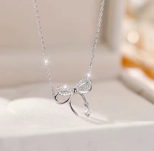 A silver bowknot necklace with zircon accents on a white surface, highlighting its elegant design and sparkling stones.