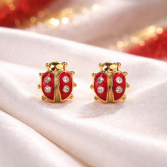 Gold and red Little Lucky Ladybug Earrings on a soft fabric background