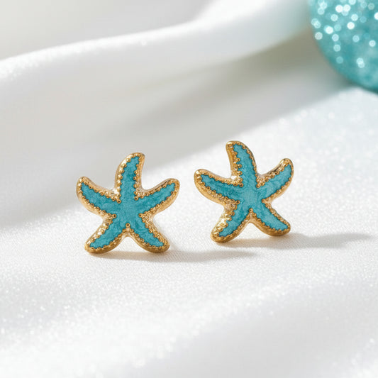 Starfish-shaped earrings with turquoise and gold details on a white cushion.