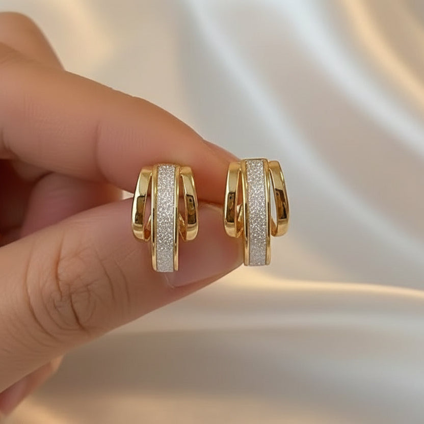 Gold Dust White & Gold Huggie Earrings with diamond accents held between fingers against a soft background