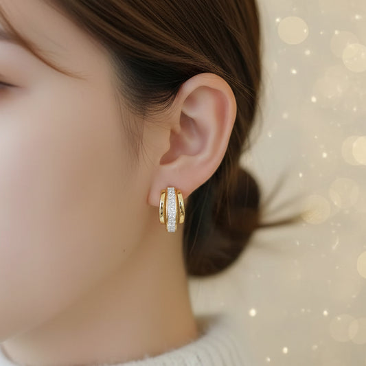 Close-up of a person wearing Gold Dust White & Gold Huggie Earrings with a neutral background