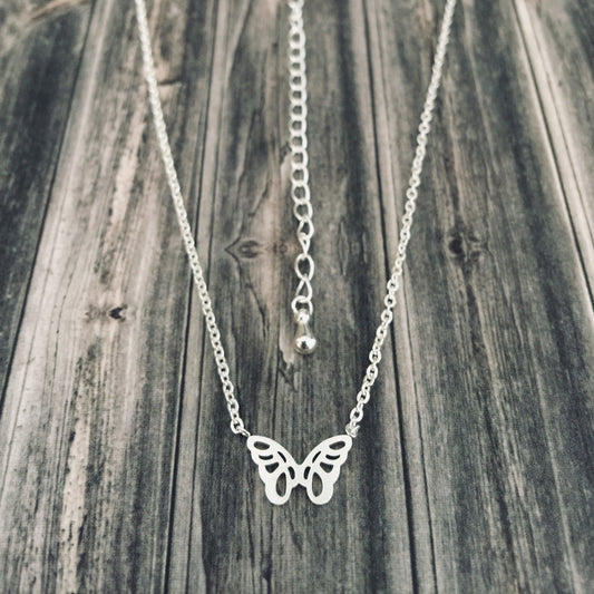 A silver necklace featuring a small origami butterfly design at the center, displayed against a wooden background.