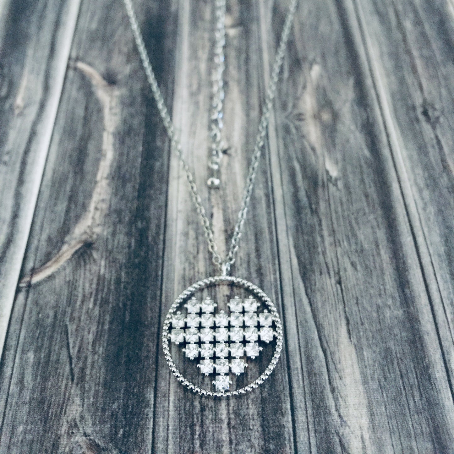 A silver rhinestone heart-shaped necklace laid out on a wooden surface.