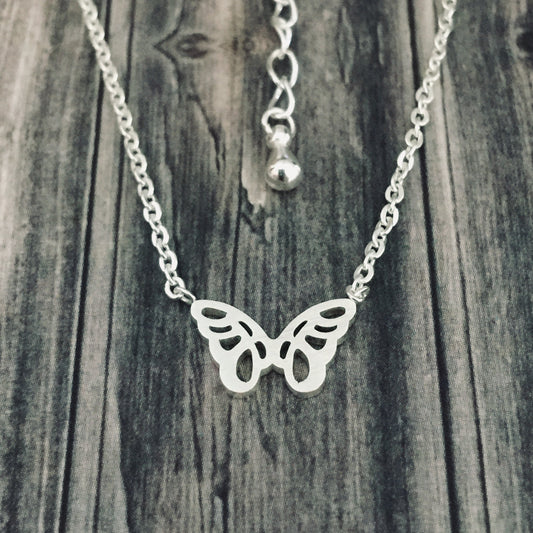 A silver necklace featuring a small origami butterfly design at the center, displayed against a wooden background.