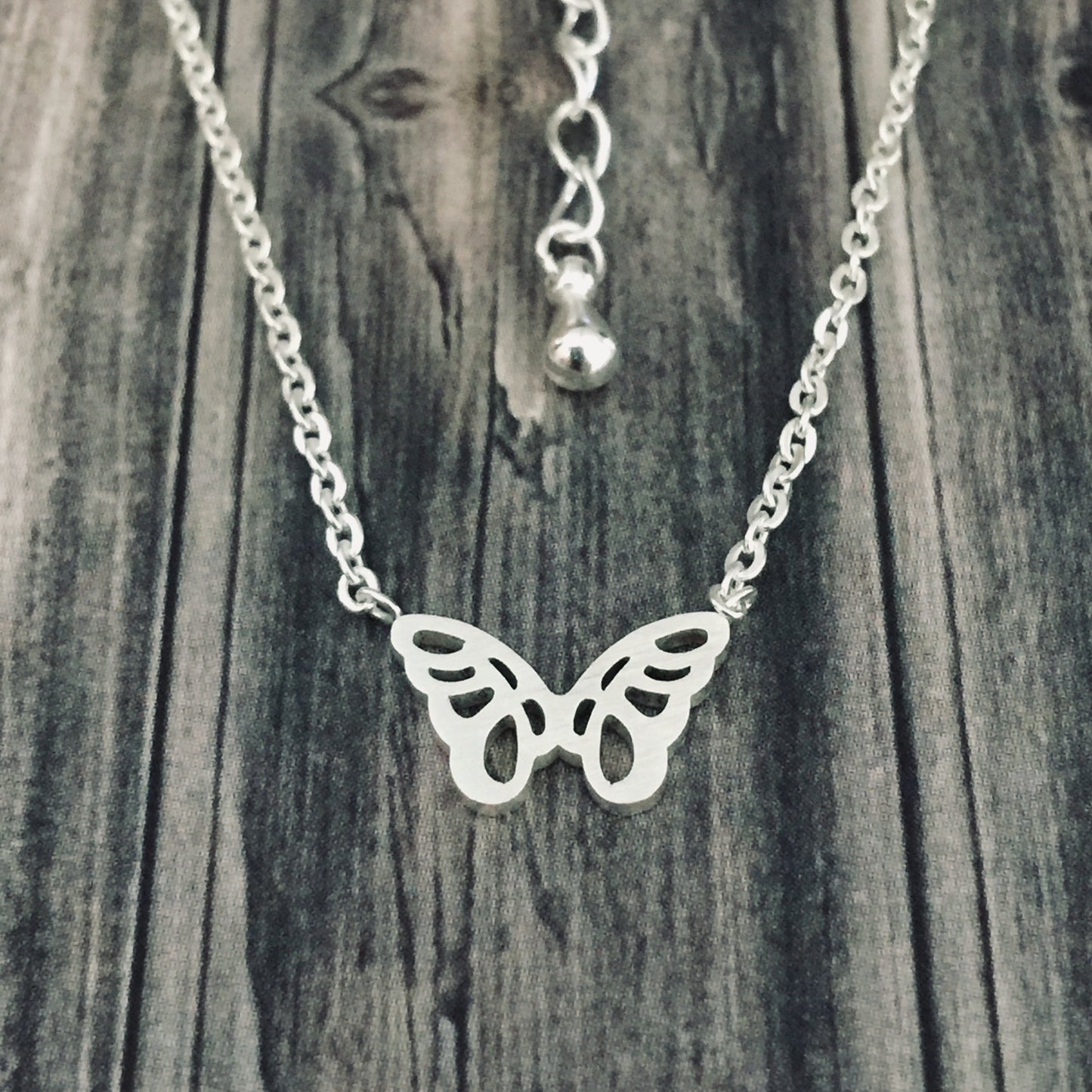 Silver Origami Butterfly Necklace displayed against a wooden background.