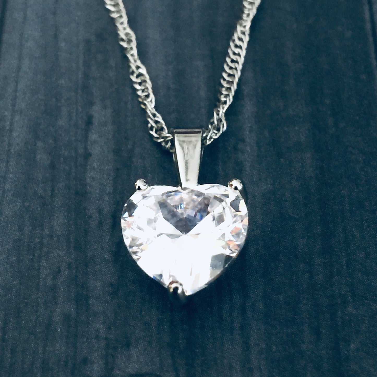 Heart-shaped crystal pendant on a chain against a dark background