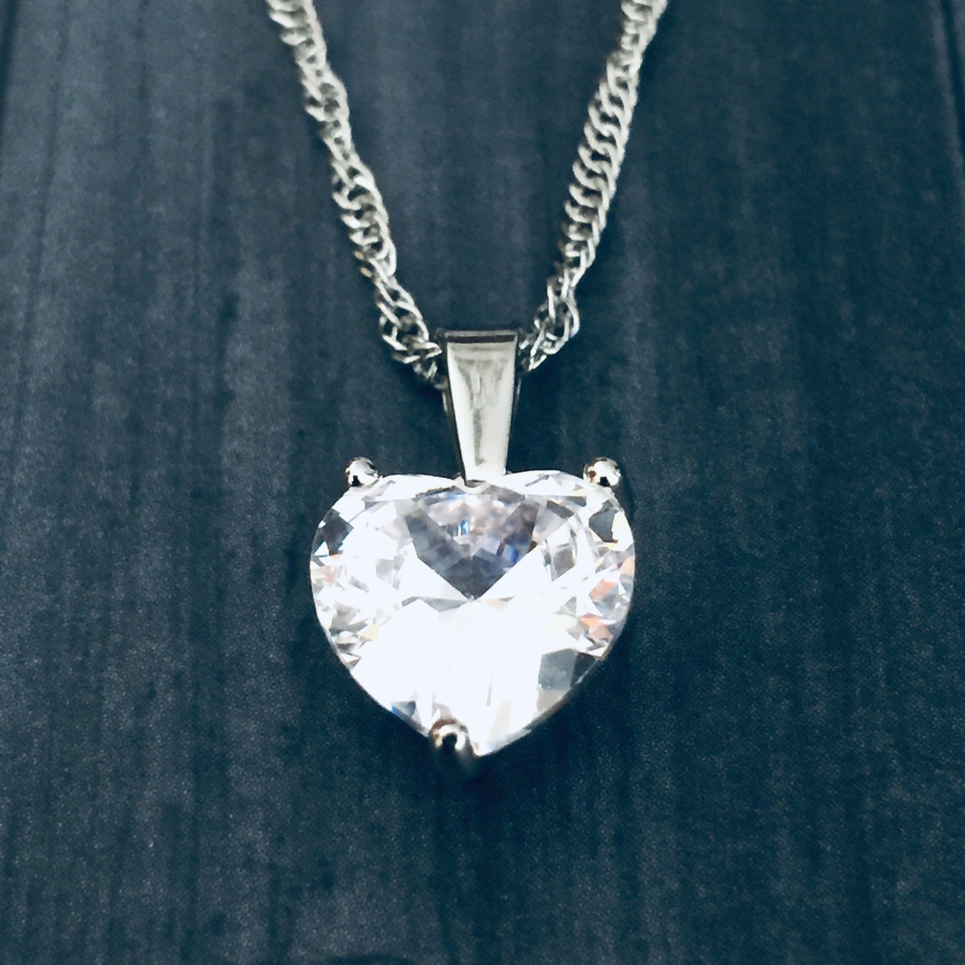 Heart-shaped crystal pendant on a chain against a dark background
