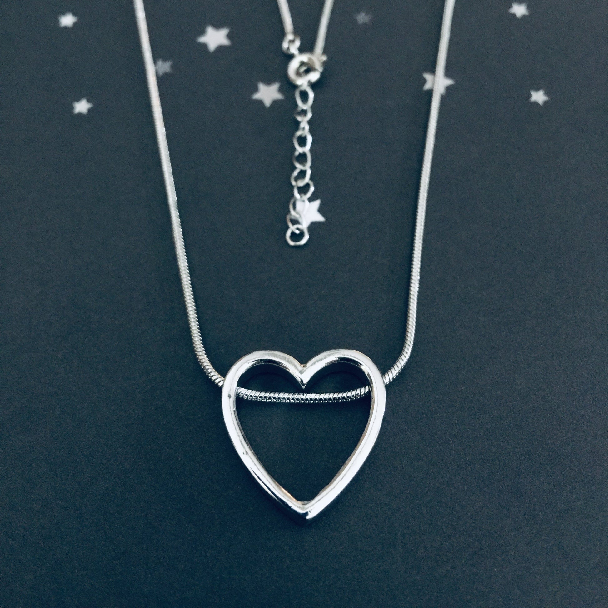 Silver heart-shaped pendant necklace on a dark background with star decorations