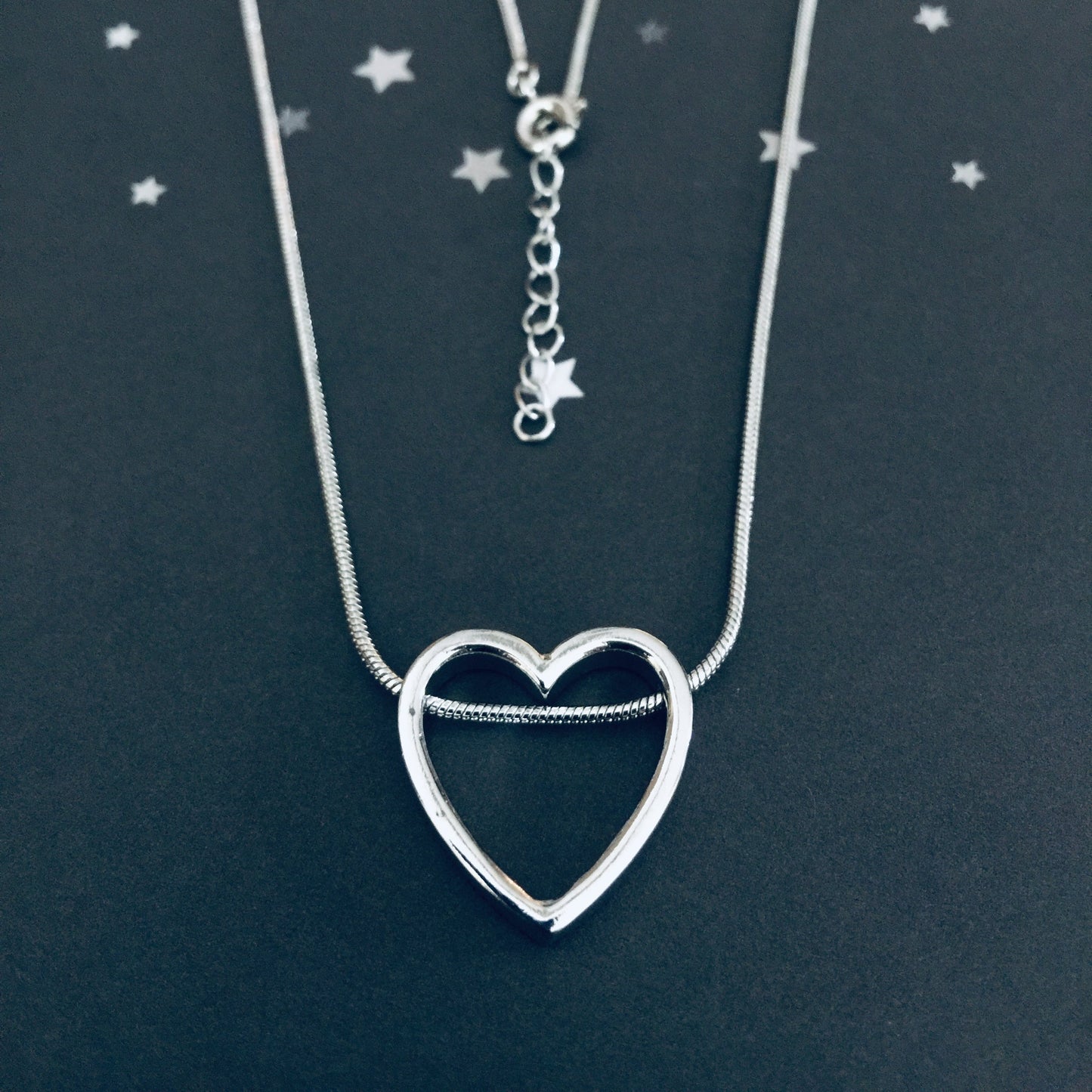 Sterling Silver Open Heart Necklace on a dark background with star decorations