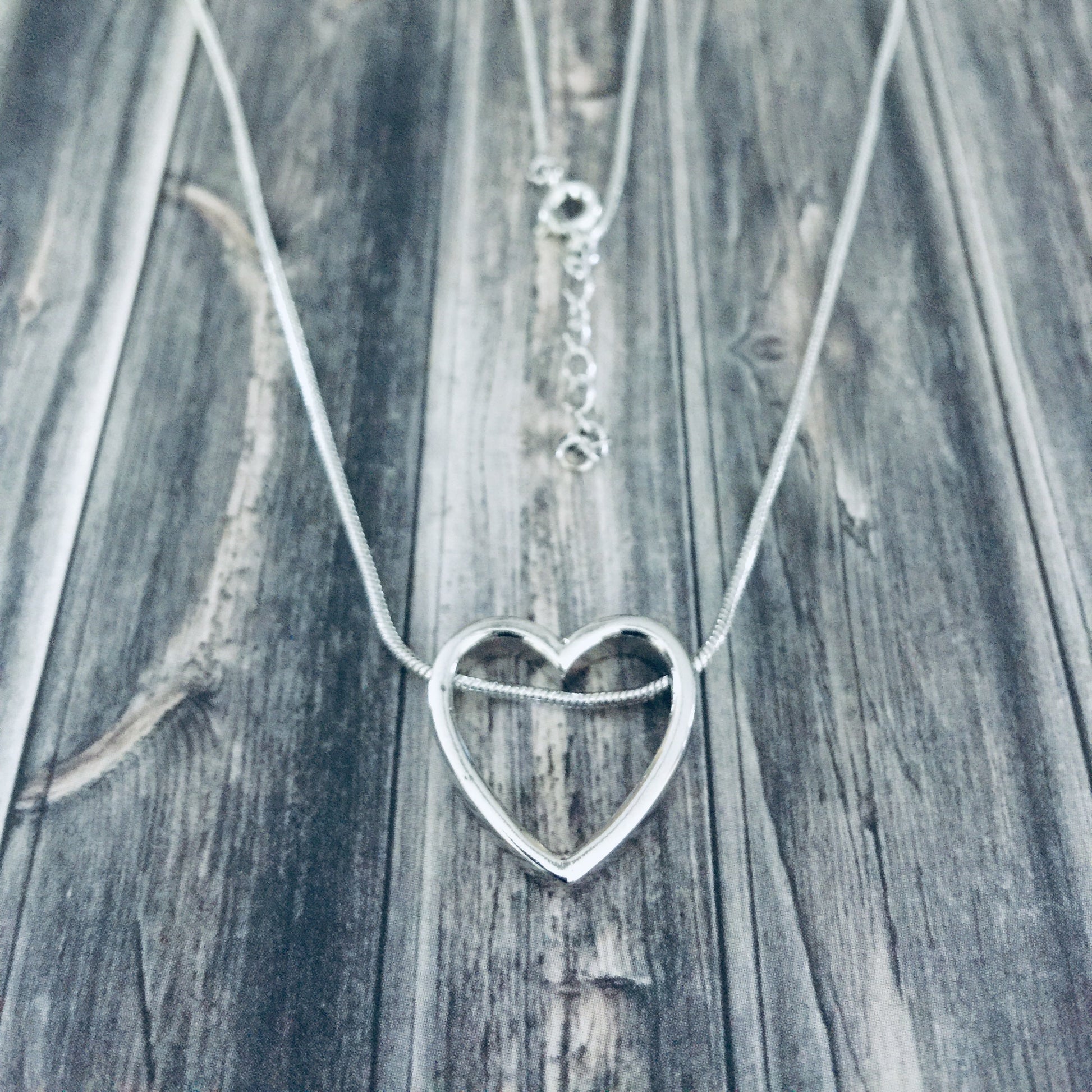 A sterling silver heart-shaped necklace laid out on a wooden surface.