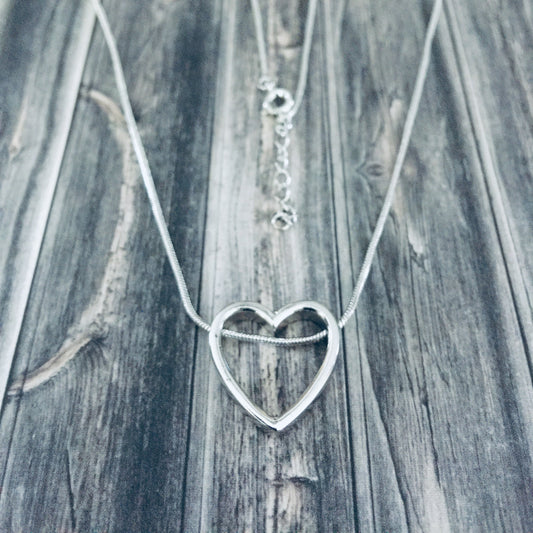 A sterling silver heart-shaped necklace laid out on a wooden surface.