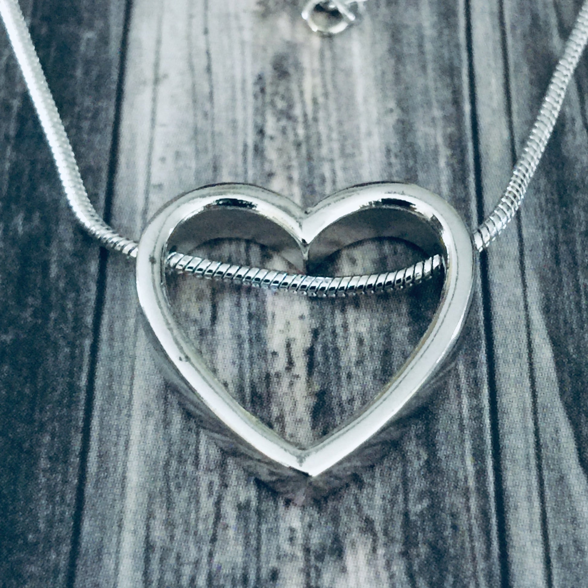 Silver heart-shaped pendant on a chain against a wooden background
