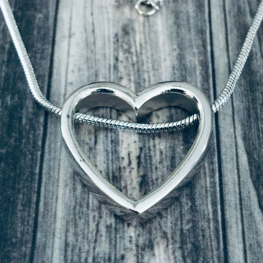 Silver heart-shaped pendant on a chain against a wooden background