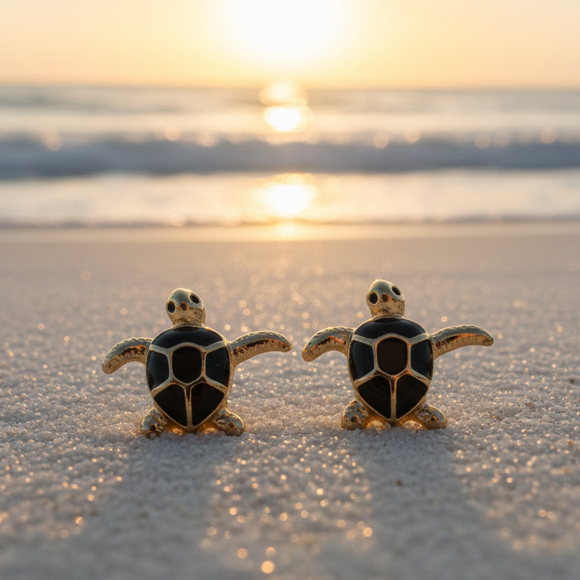 Black & Gold Sea Turtle Earrings on a sandy beach with a sunset in the background