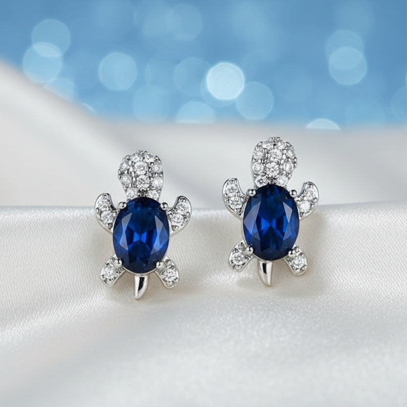 Blue Crystal Turtle Earrings with blue gemstones on a white surface with a blue blurred background