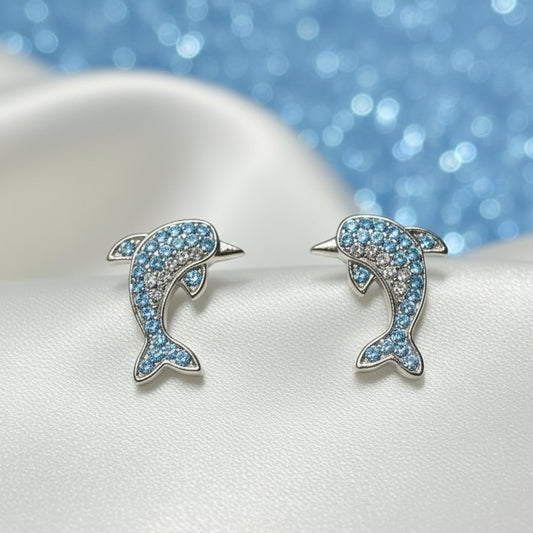 Blue Pavé Dolphin Earrings on a white surface with a blue glittery background