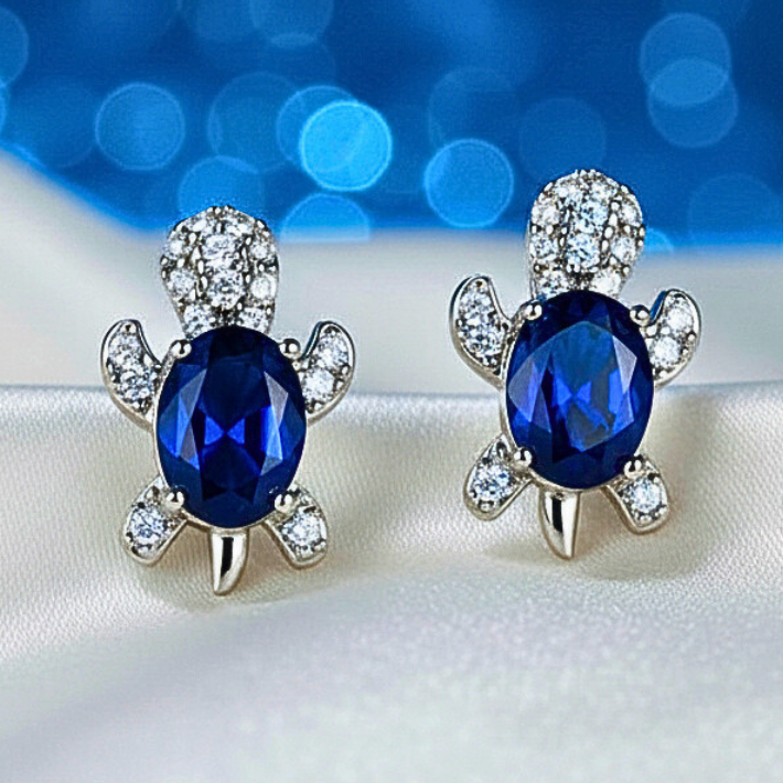 Blue Crystal Turtle Earrings with blue gemstones on a white fabric background