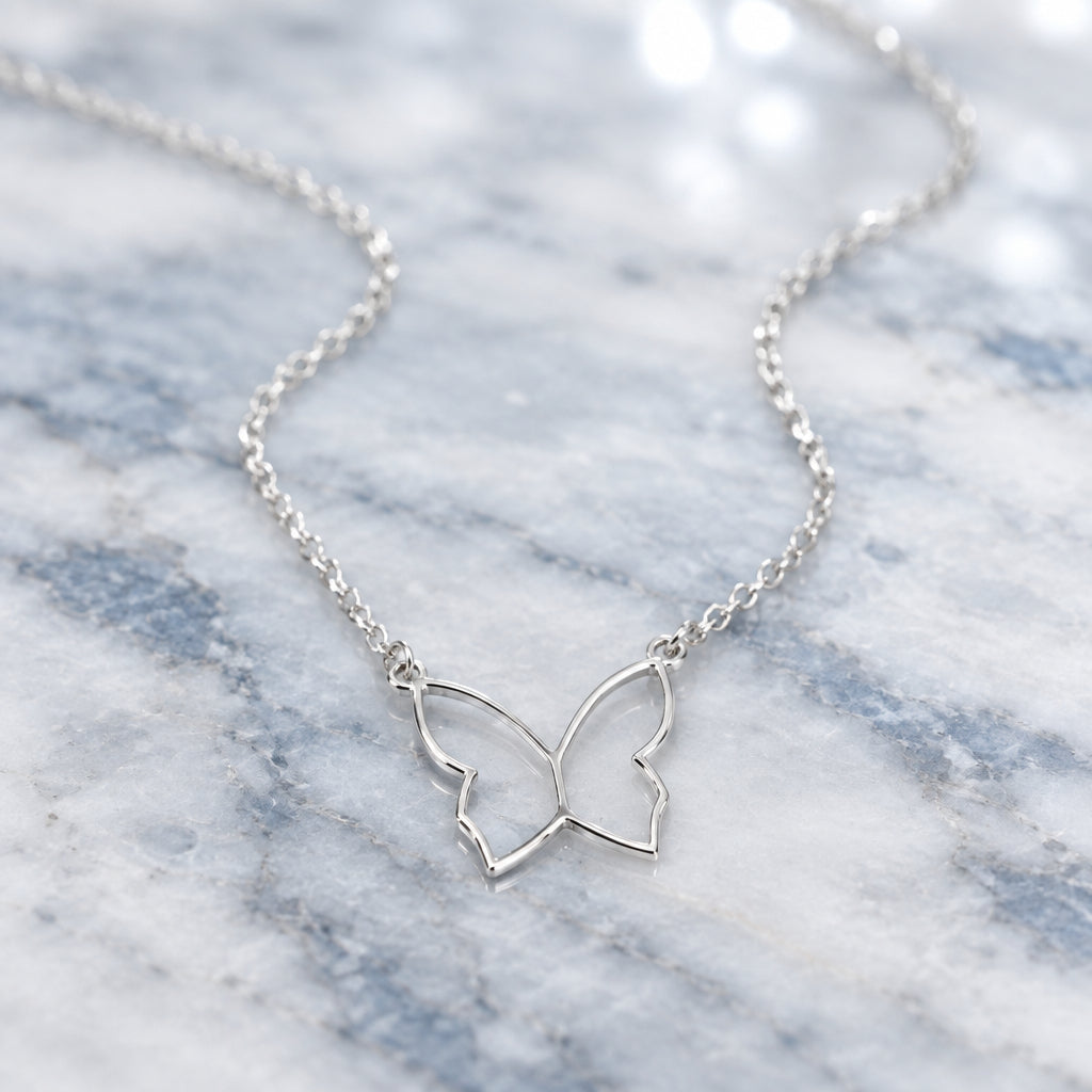 A delicate silver butterfly pendant necklace on a fine link chain, displayed on marble