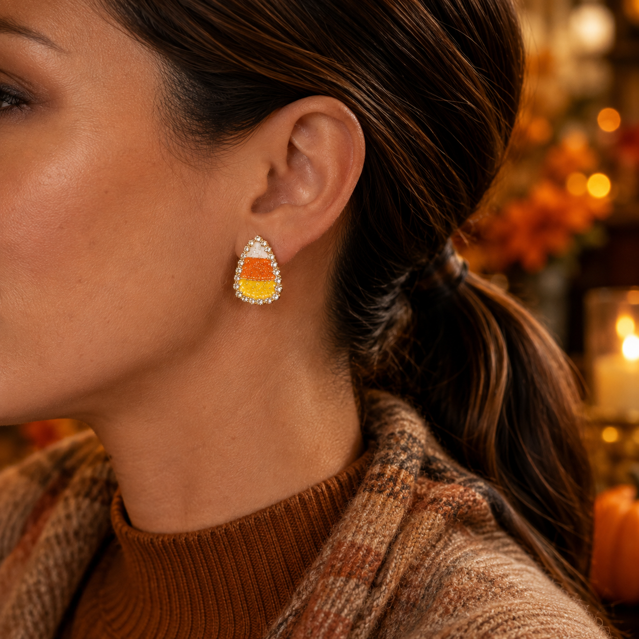 A close-up of a woman wearing a Candy Corn Rhinestone Earrings, set with small clear stones and gold-toned metal.