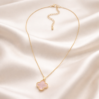Pink Clover Gold Necklace with a pink clover pendant on a beige fabric background