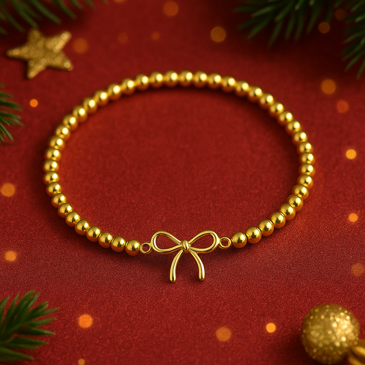 Gold Bow Bead Bracelet with a bow charm on a red background with Christmas decorations.