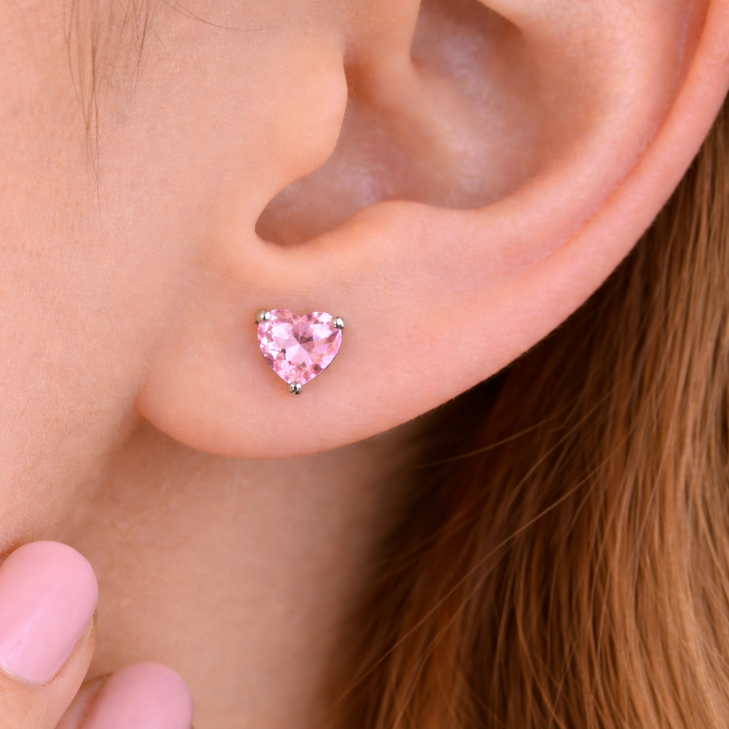 Heart-shaped pink earrings worn by a person with light skin and brown hair.