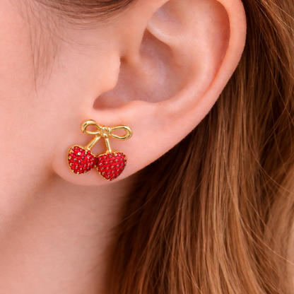 Close-up of an ear wearing red cherry earrings with a gold bow.
