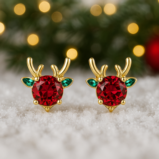 Holiday Red & Green Reindeer Stud Earrings with red gemstones on a snowy surface with Christmas tree background.
