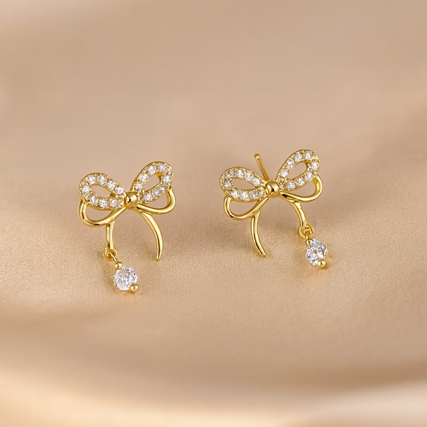 Sparkling Gold Crystal Bow Earrings with small diamonds on a beige background