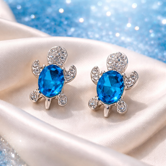Ocean Blue Crystal Turtle Earrings with blue gemstones on a white fabric background