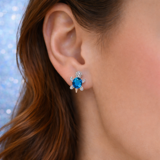 Close-up of an ear wearing a Ocean Blue Crystal Turtle Earring with a blurred background