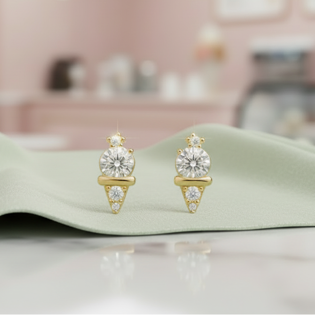 Gold earrings with clear gemstones on a reflective surface with a blurred pink room background