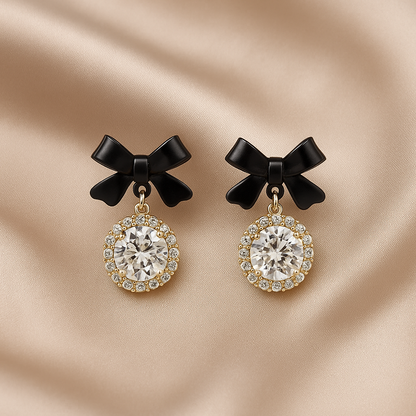 Pair of Black Bow Crystal Drop Earrings on a beige fabric background