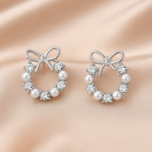 Pair of Silver Bow Wreath Earrings with bow and pearl design on a beige background