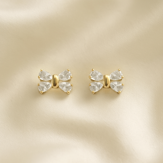 Mini Crystal Bow Earrings with clear gemstones on a beige satin background