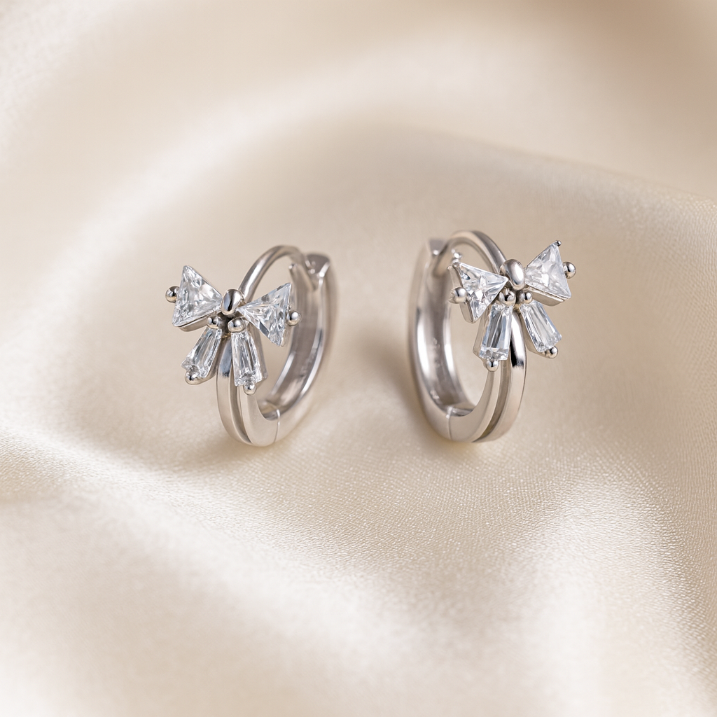 Tiny Crystal Ribbon Earrings with bow-shaped diamond accents on a beige satin background