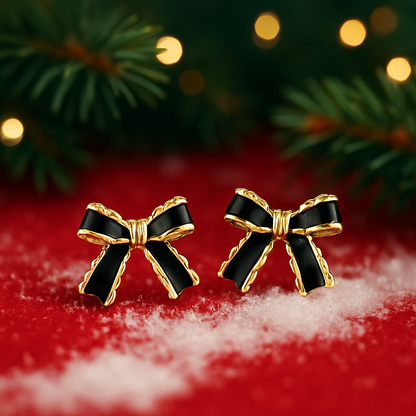 Black & Gold Bow Earrings on a red surface with Christmas tree branches and lights in the background.