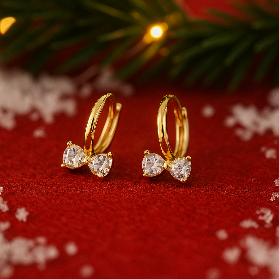Gold Zircon Bow Hoop Earrings on a red surface with snowflakes and greenery.