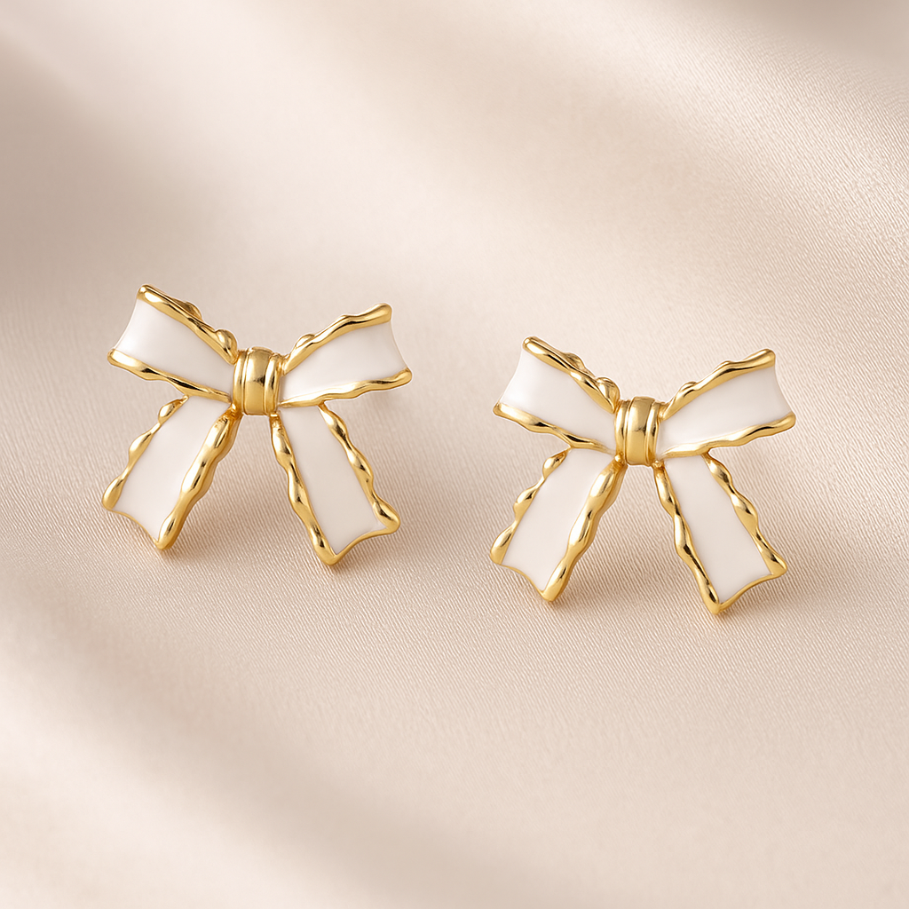 White and Gold Bow Earrings with gold accents on a beige fabric background