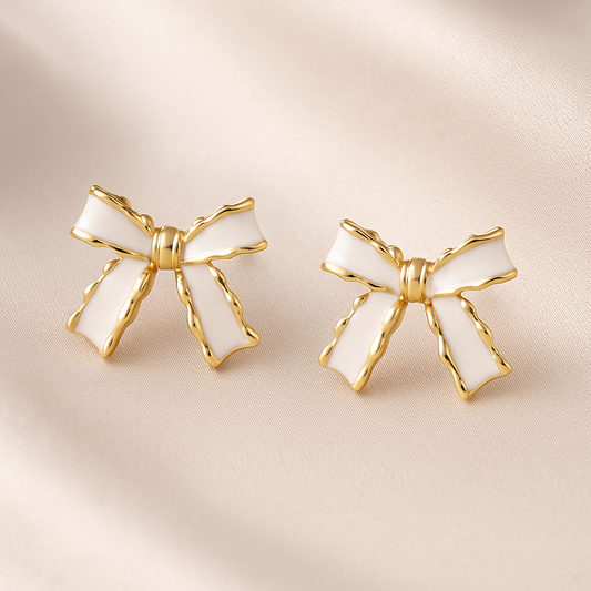 White and Gold Bow Earrings with gold accents on a beige fabric background