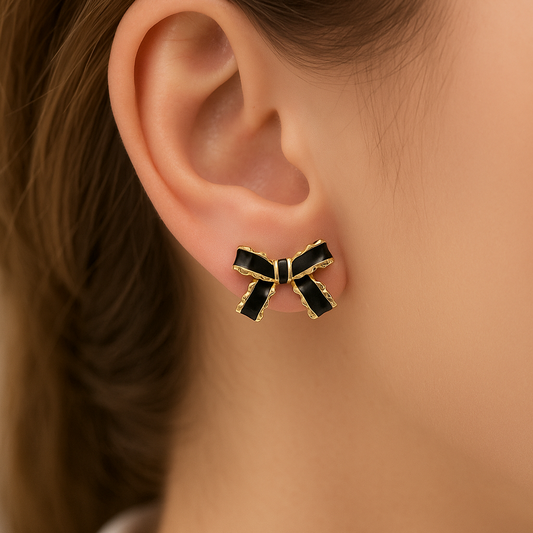 Black and Gold Bow Earrings on a person's ear with a neutral background