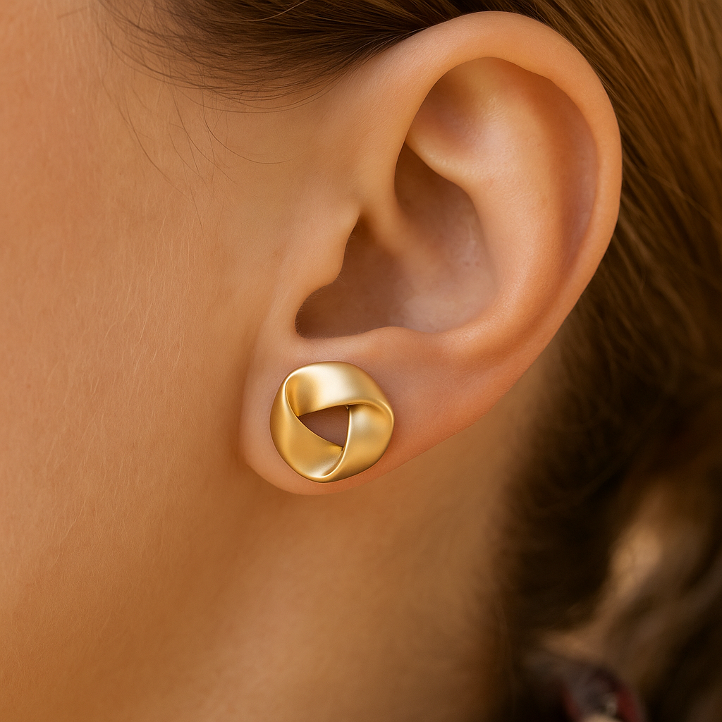 satin gold knot earrings worn on a woman's ear with a blurred background