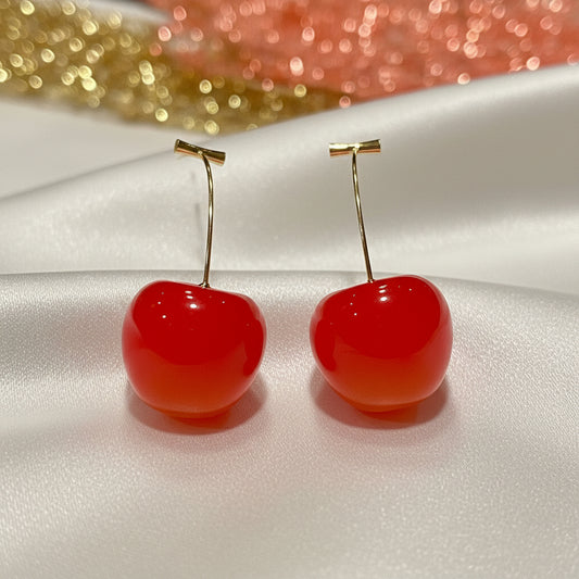 Coral Cherry Drop Earrings on a reflective surface with a glittery background