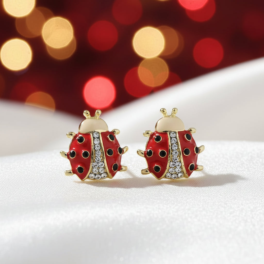 Crystal Accent Ladybug Earrings with gold accents on a white surface with blurred lights in the background