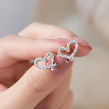 Crystal Open Heart Earrings held between fingers with a blurred background
