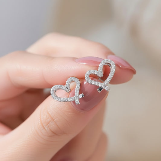 Crystal Open Heart Earrings held between fingers with a blurred background