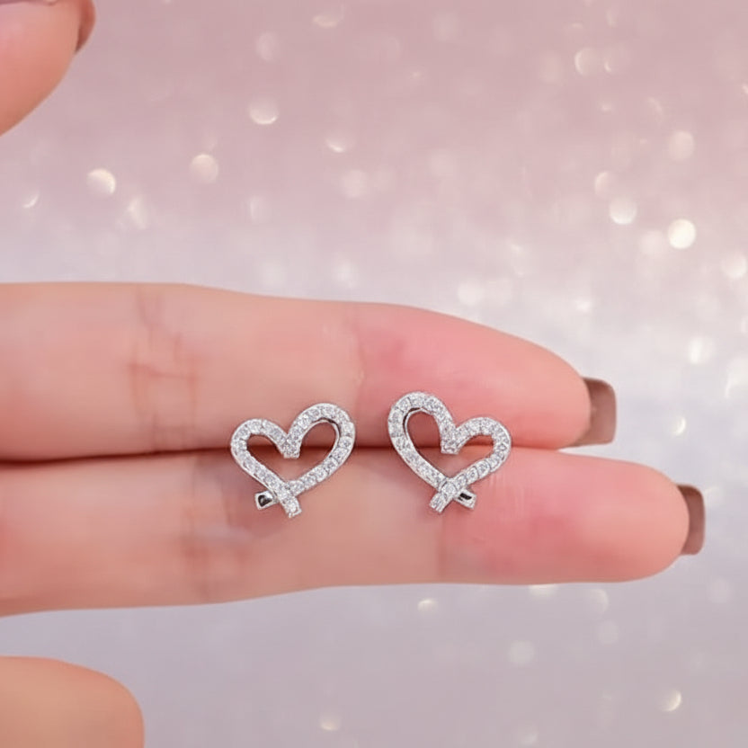 Crystal Open Heart Earrings held between two fingers against a soft background